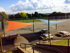 Photo of two triangle shade sails installed between wooden posts. Orange and blue shade sail.