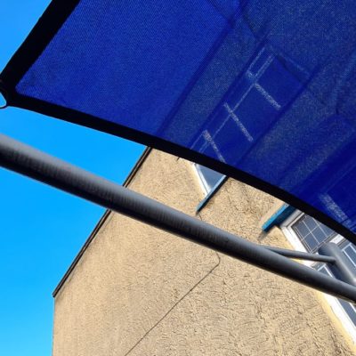 Close up photo of a blue rectangular shade sail installed on school building