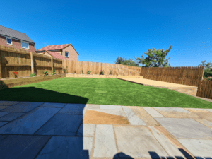 Photo of a garden with raj green Indian stone patio, artificial turf, raised decking, and a raised sleeper planter border