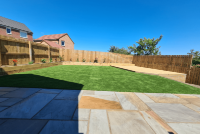 Photo of a garden with raj green Indian stone patio, artificial turf, raised decking, and a raised sleeper planter border