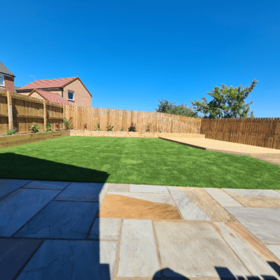Photo of a garden with raj green Indian stone patio, artificial turf, raised decking, and a raised sleeper planter border