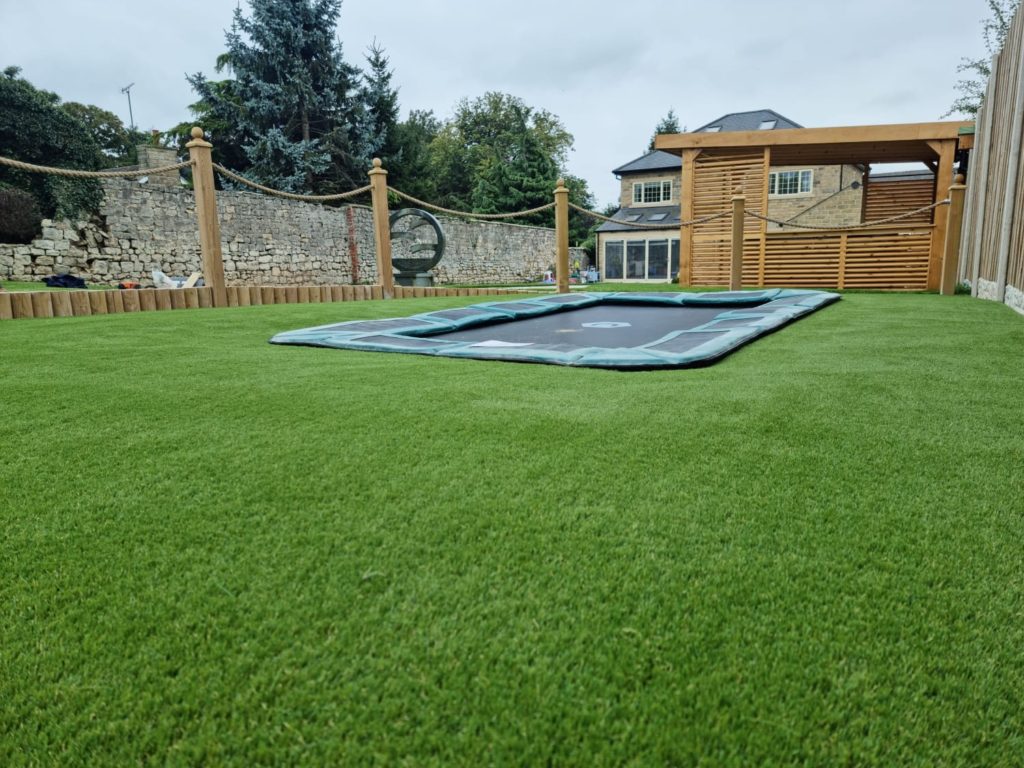 Artificial grass install in Doncaster, with sunken trampoline and rising log border and rope surround