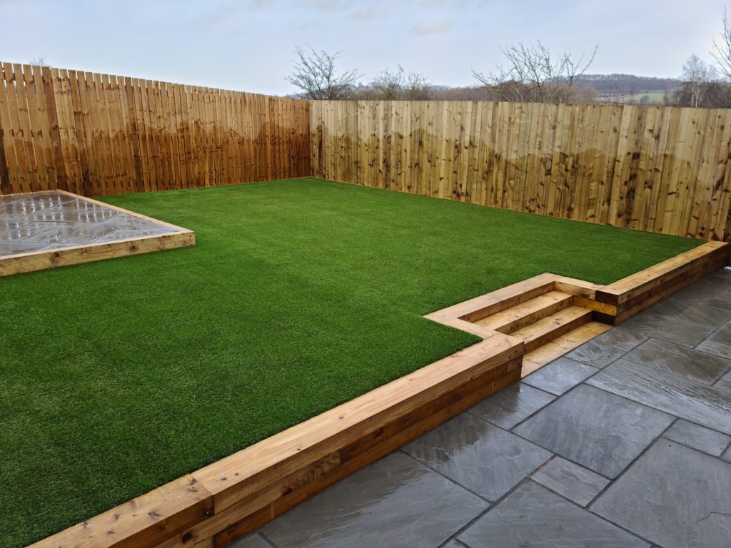 Photo of garden with Indian stone patio, and raised seating area, retaining sleeper wall, and artificial turf