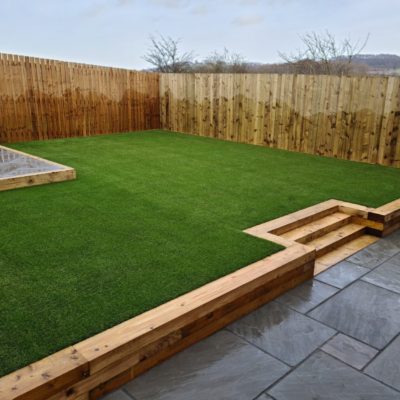 Photo of garden with Indian stone patio, and raised seating area, retaining sleeper wall, and artificial turf