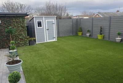 Photo of back garden fake turf install in Barnsley, with grey composite fence and matching shed