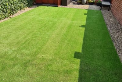 Photo of back garden on a sunny day in Barnsley, with artificial grass, shrubs to one side and a shed at the back