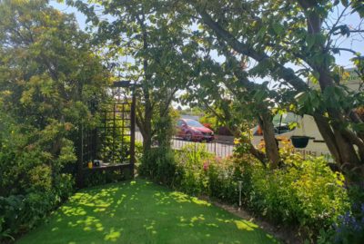 Photo of front garden artificial turf install in Barnsley, South Yorkshire, surrounded by crowding trees and a small pergola