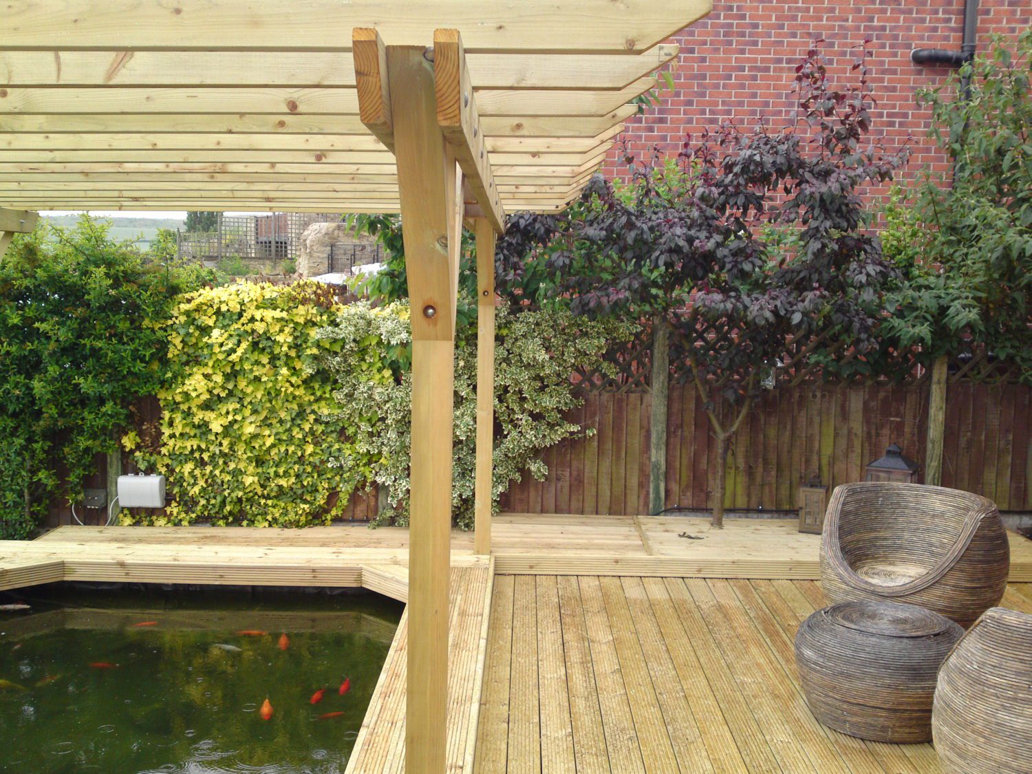 Photo of a decking and pergola installation over a pond, by Greenfield Leisure in Rotherham. With some rattan furniture