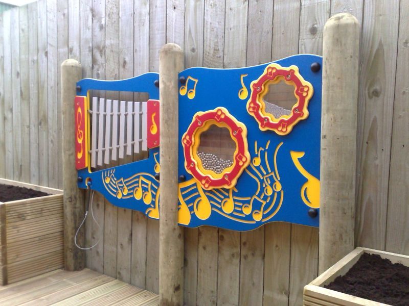 Closeup photo of HDPE musical instrument play panels between 3 logs, one chimes panel, and one shaker panel